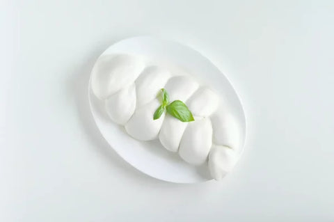 Treccia di mozzarella di bufala campana DOP su piatto bianco con foglie di basilico fresco